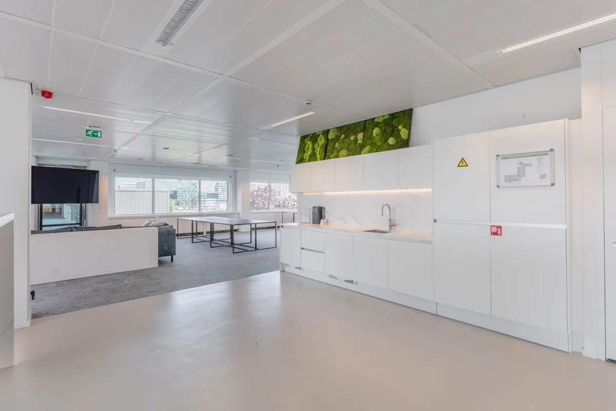 Moderne kantoorkeuken aan de Laarderhoogtweg met witte kasten, groene moswand en uitzicht op de stad.
