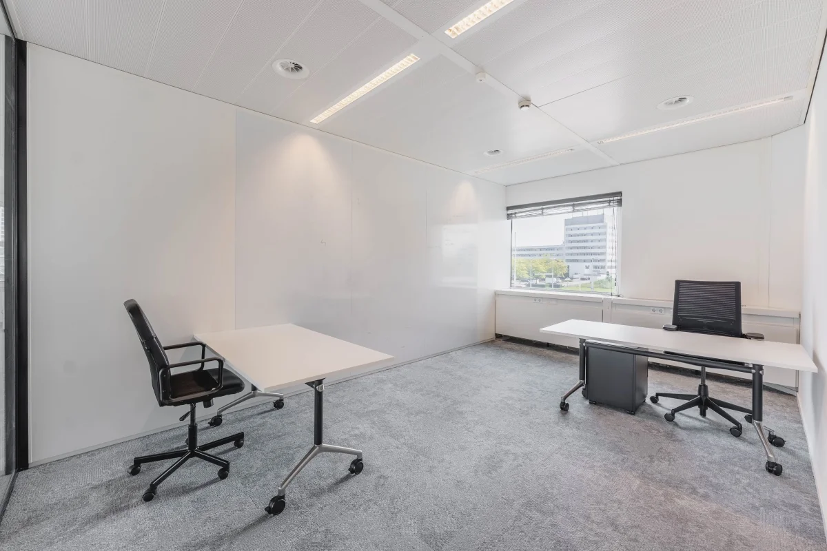 Lichte en moderne kantoorruimte aan de Laarderhoogtweg met twee bureaus, bureaustoelen en uitzicht op een kantoorgebouw.
