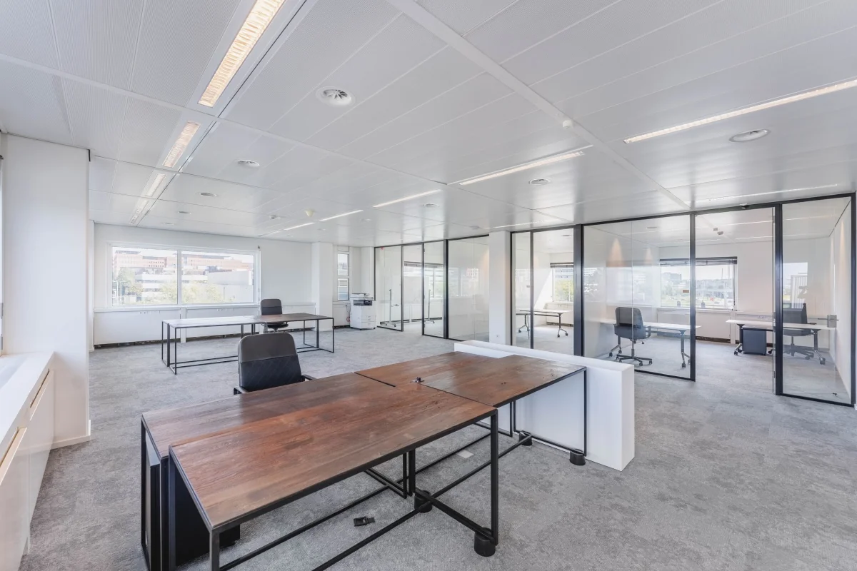 Modern, licht kantoorinterieur aan de Laarderhoogtweg met glazen vergaderruimtes en houten bureaus.