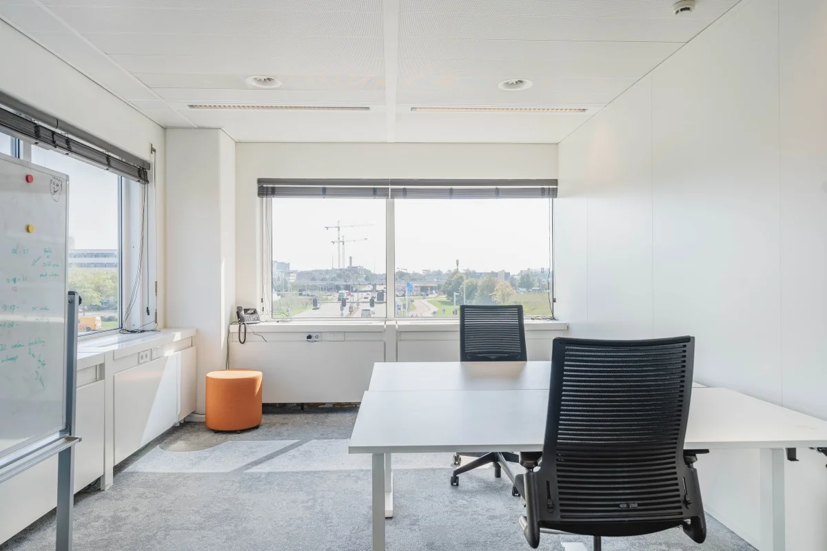 Lichte kantoorruimte aan de Laarderhoogtweg met twee bureaustoelen, groot raam en uitzicht op een stedelijke omgeving.