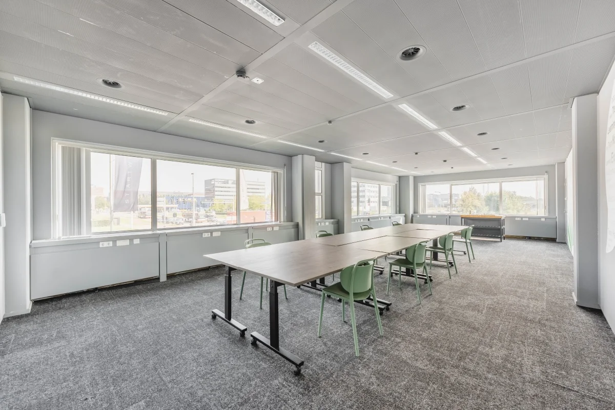 Licht en modern vergaderruimte-interieur aan de Laarderhoogtweg met lange tafel, groene stoelen en grote ramen met stadsuitzicht.