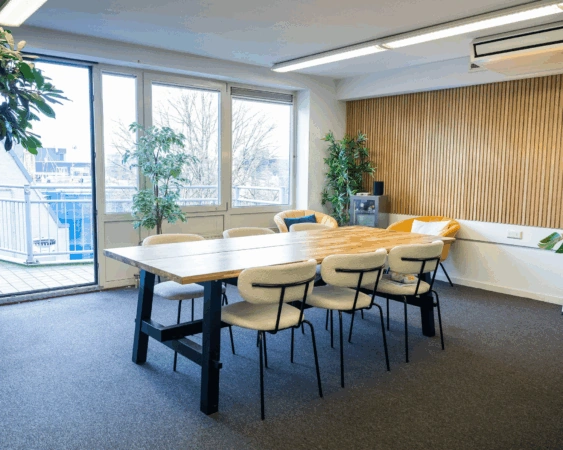 Vergaderruimte aan de Prins Hendrikkade met houten tafel, moderne stoelen, planten en uitzicht op het balkon.