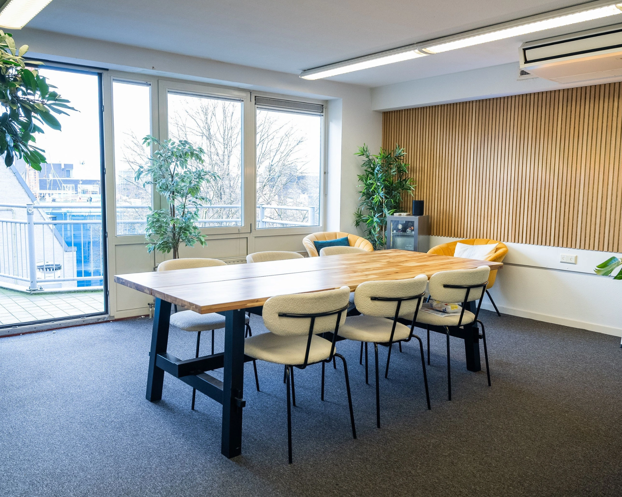 Vergaderruimte aan de Prins Hendrikkade met houten tafel, moderne stoelen, planten en uitzicht op het balkon.