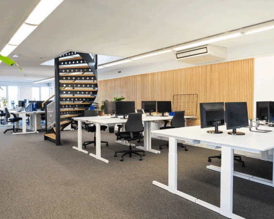 Moderne open kantoorruimte aan de Prins Hendrikkade met bureaus, bureaustoelen, computerschermen en een zwarte wenteltrap.