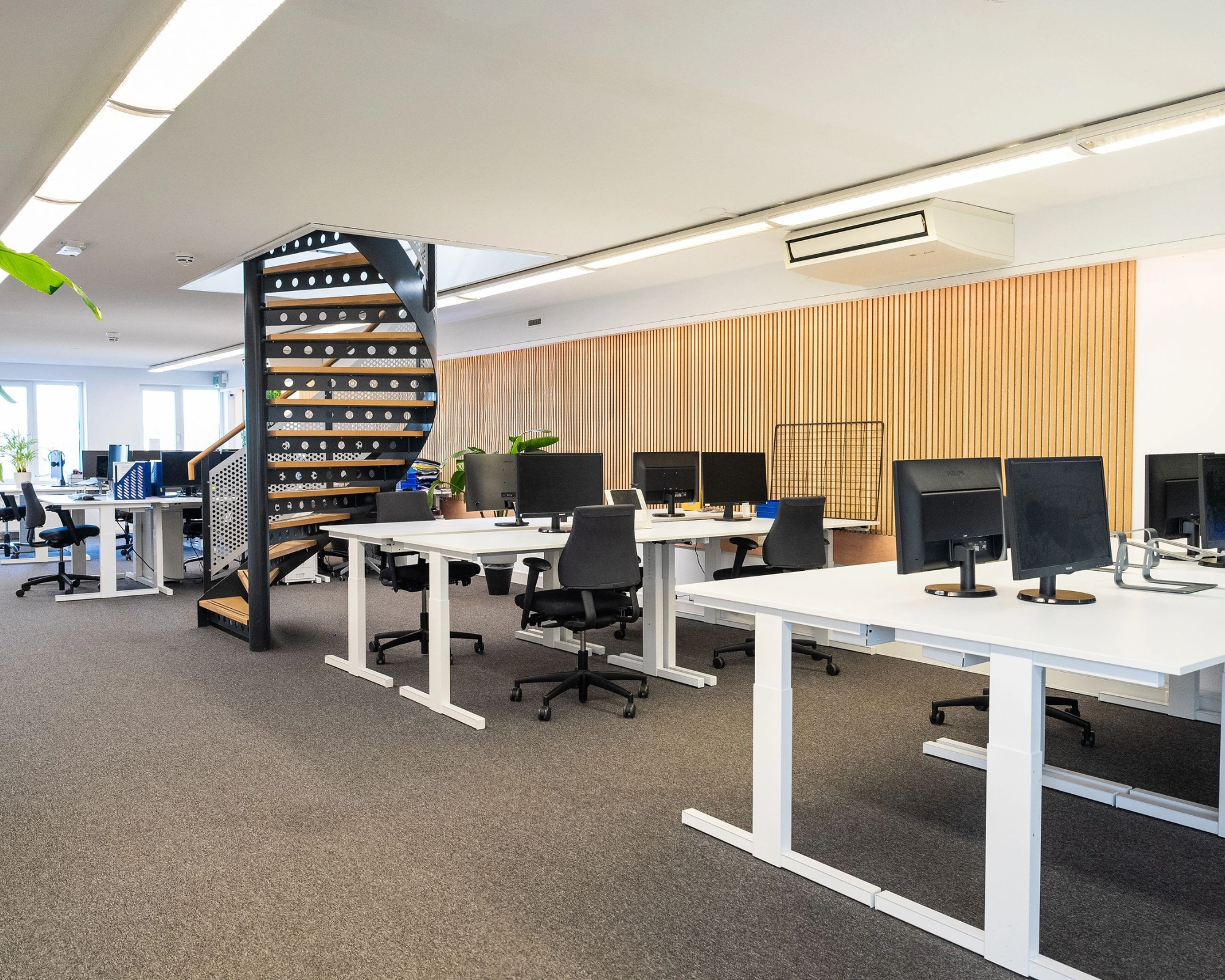Moderne open kantoorruimte aan de Prins Hendrikkade met bureaus, bureaustoelen, computerschermen en een zwarte wenteltrap.