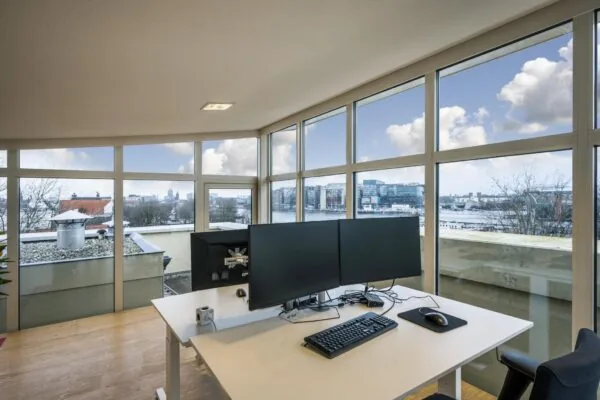 Modern kantoor met dubbele monitoren en panoramisch uitzicht op de Prins Hendrikkade in Amsterdam.