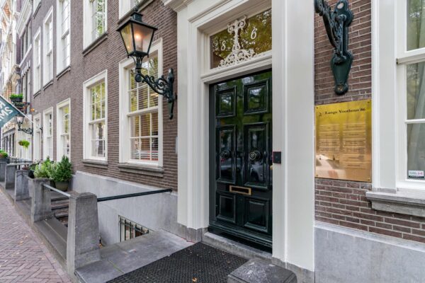 Ingang van een klassiek herenhuis aan Lange Voorhout 86 met zwarte voordeur, gevelbord en smeedijzeren lantaarns.