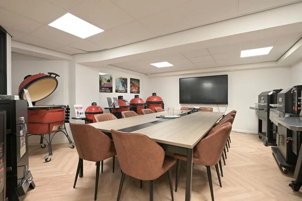 Vergaderruimte met moderne kookapparatuur en meerdere rode Kamado barbecues langs de muur.