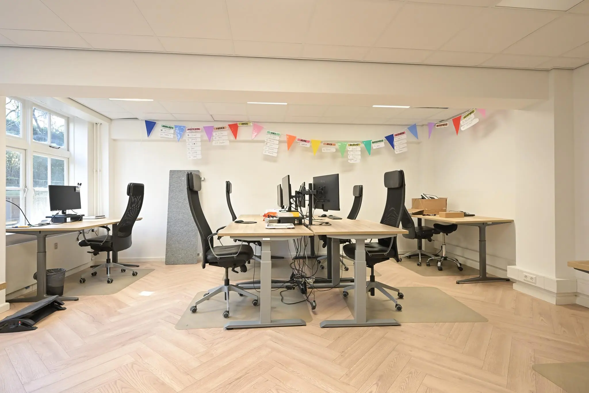 Moderne kantoorruimte aan het Lange Voorhout met bureaus, ergonomische stoelen en kleurrijke vlaggetjes aan de muur.