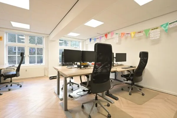 Modern kantoor met ergonomische bureaustoelen, meerdere computerschermen en kleurrijke slingers aan de muur op Lange Voorhout.