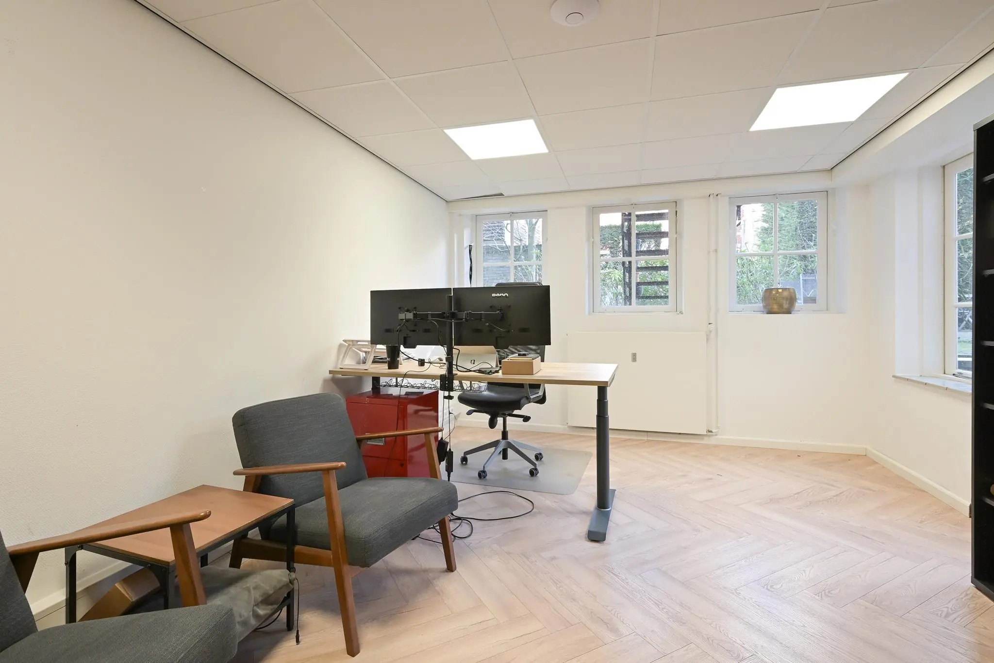 Lichte kantoorruimte aan het Lange Voorhout met bureau, dubbele monitoren en twee grijze stoelen.