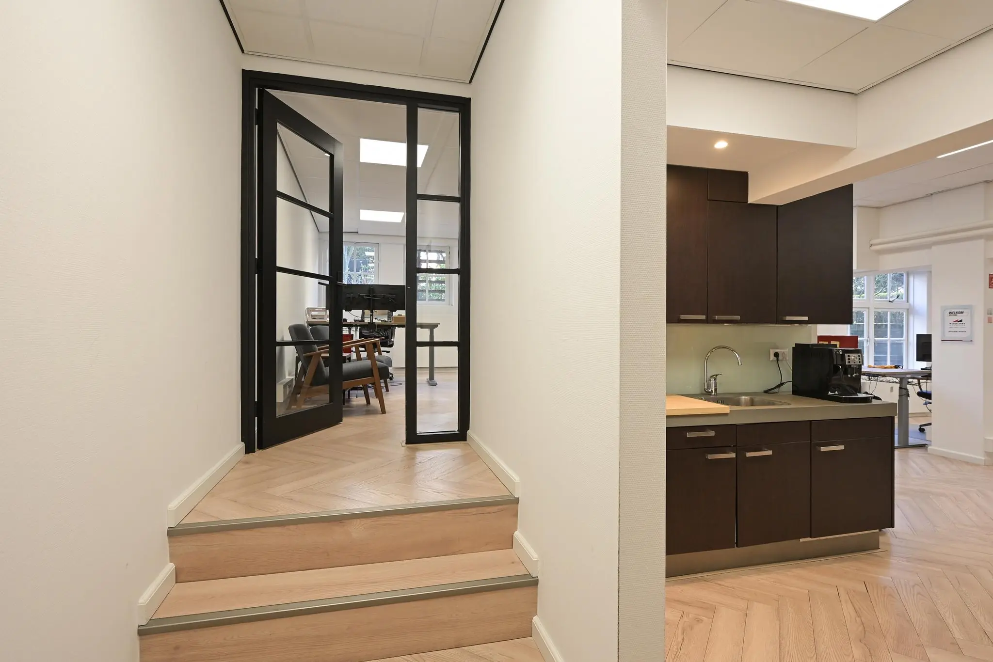 Moderne kantoorruimte in Lange Voorhout met houten vloer, glazen deur en een kitchenette.