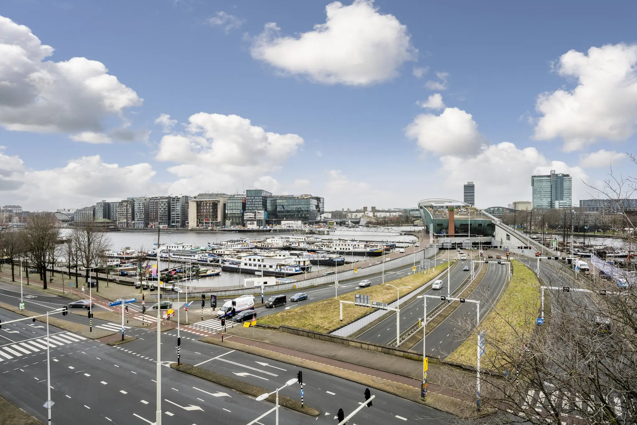 Panoramisch uitzicht op de Prins Hendrikkade in Amsterdam met het NEMO Science Museum, het IJ en aangemeerde boten.