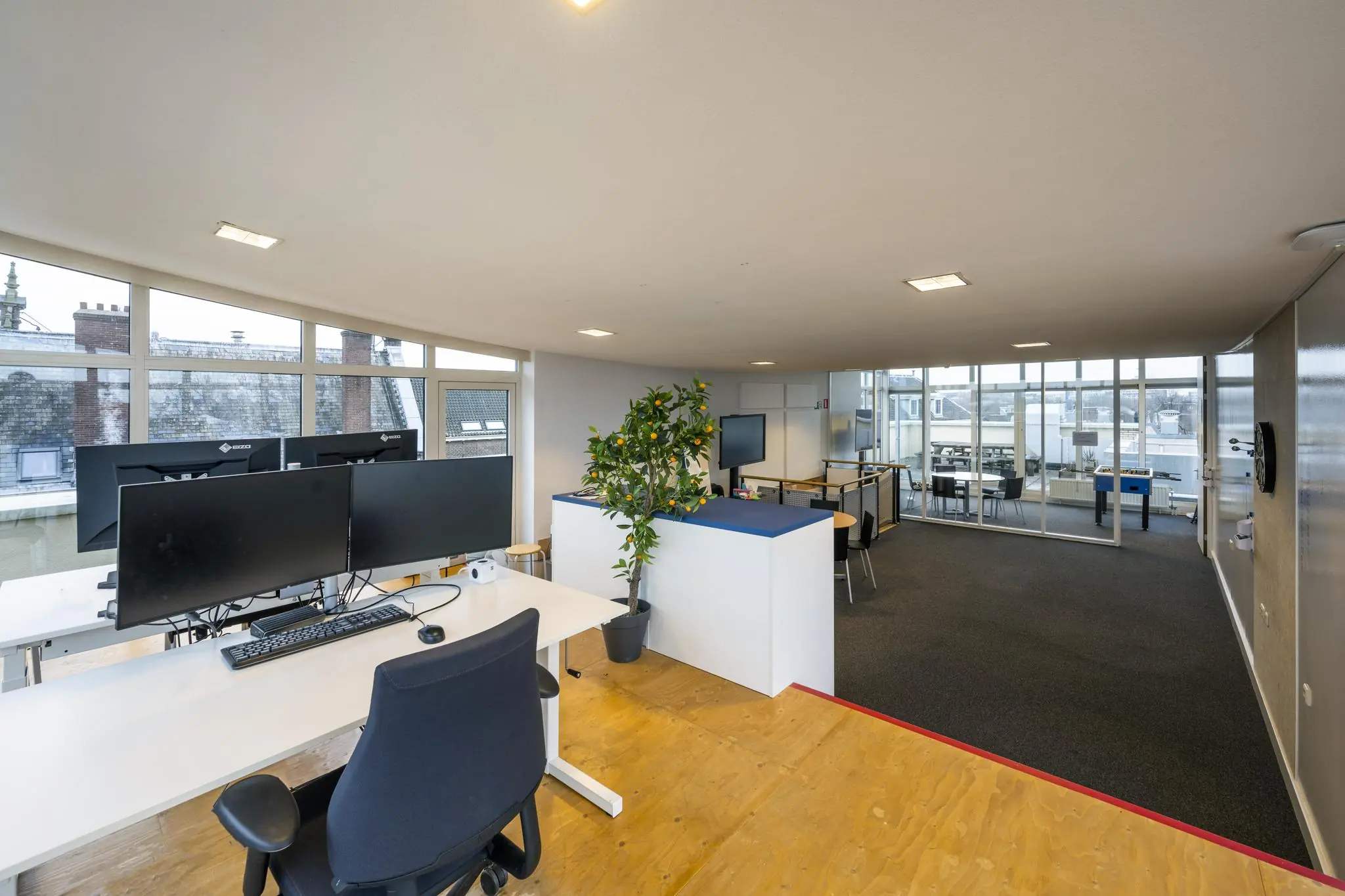 Modern kantoorinterieur aan de Prins Hendrikkade met werkplekken, glazen vergaderruimte en uitzicht op historische daken.