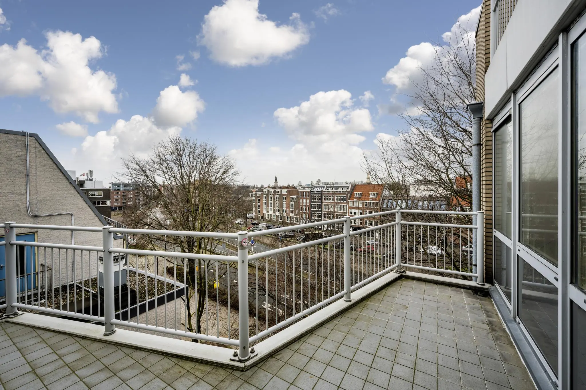 Balkon met uitzicht op de Prins Hendrikkade en omliggende bebouwing onder een deels bewolkte hemel.