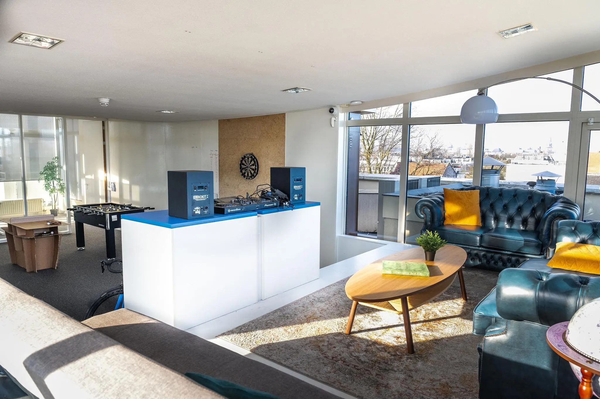 Moderne lounge met leren banken, DJ-set, tafelvoetbaltafel en uitzicht op de Prins Hendrikkade.