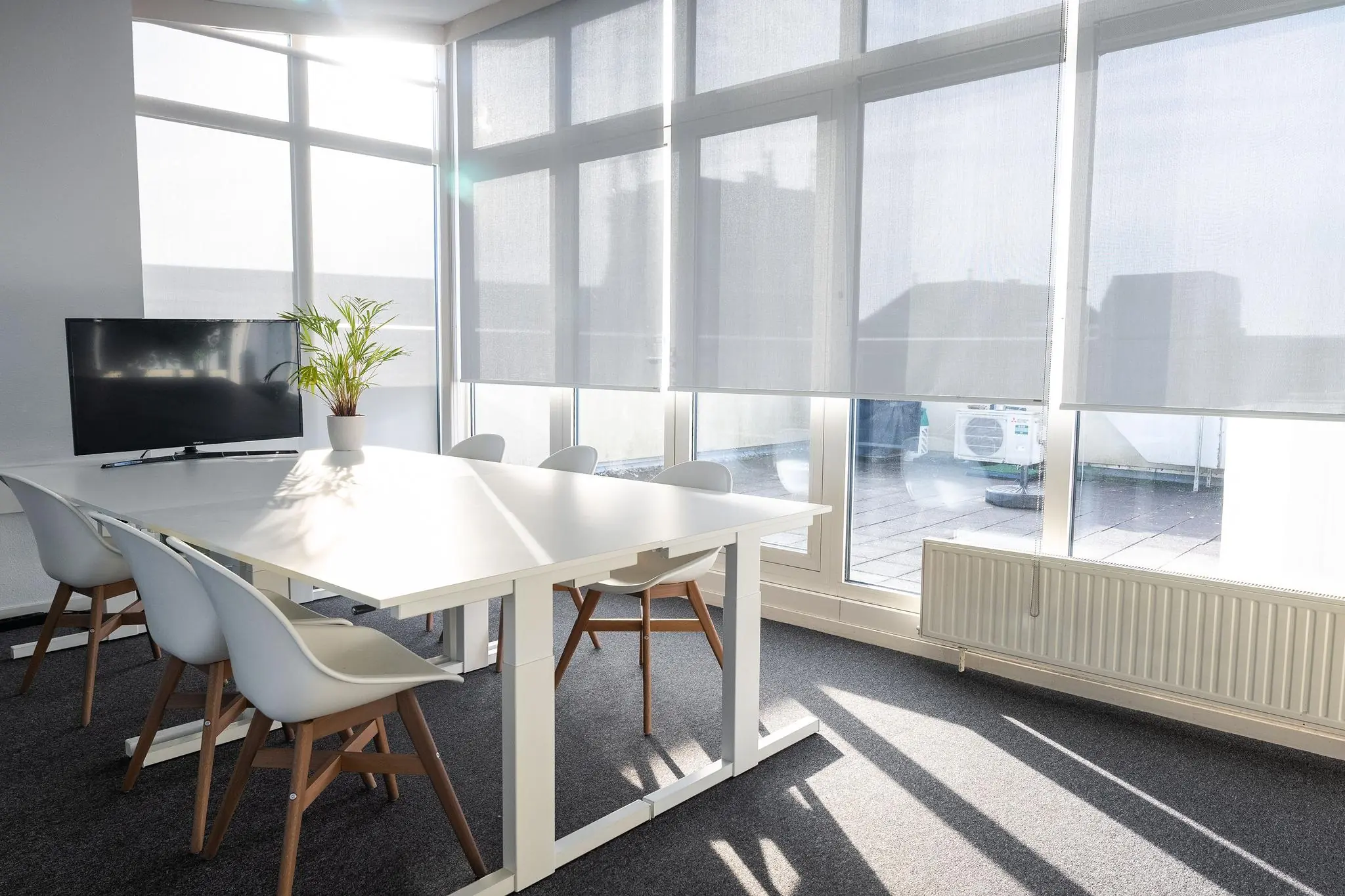 Moderne, lichte vergaderruimte aan de Prins Hendrikkade met witte meubels, een flatscreen en grote ramen met zonwering.
