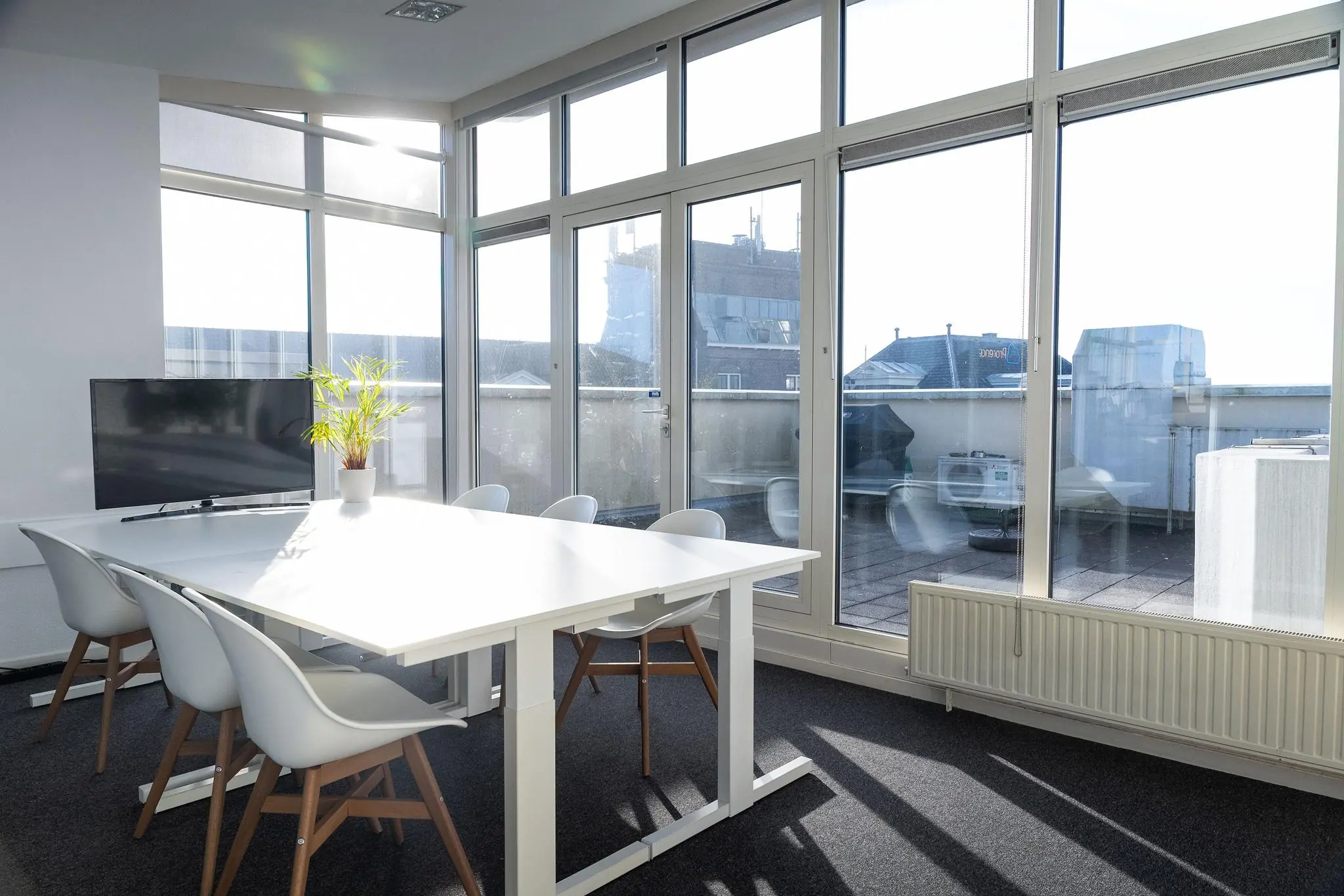 Lichte vergaderruimte aan de Prins Hendrikkade met grote ramen, moderne stoelen, een witte tafel en uitzicht op een dakterras.