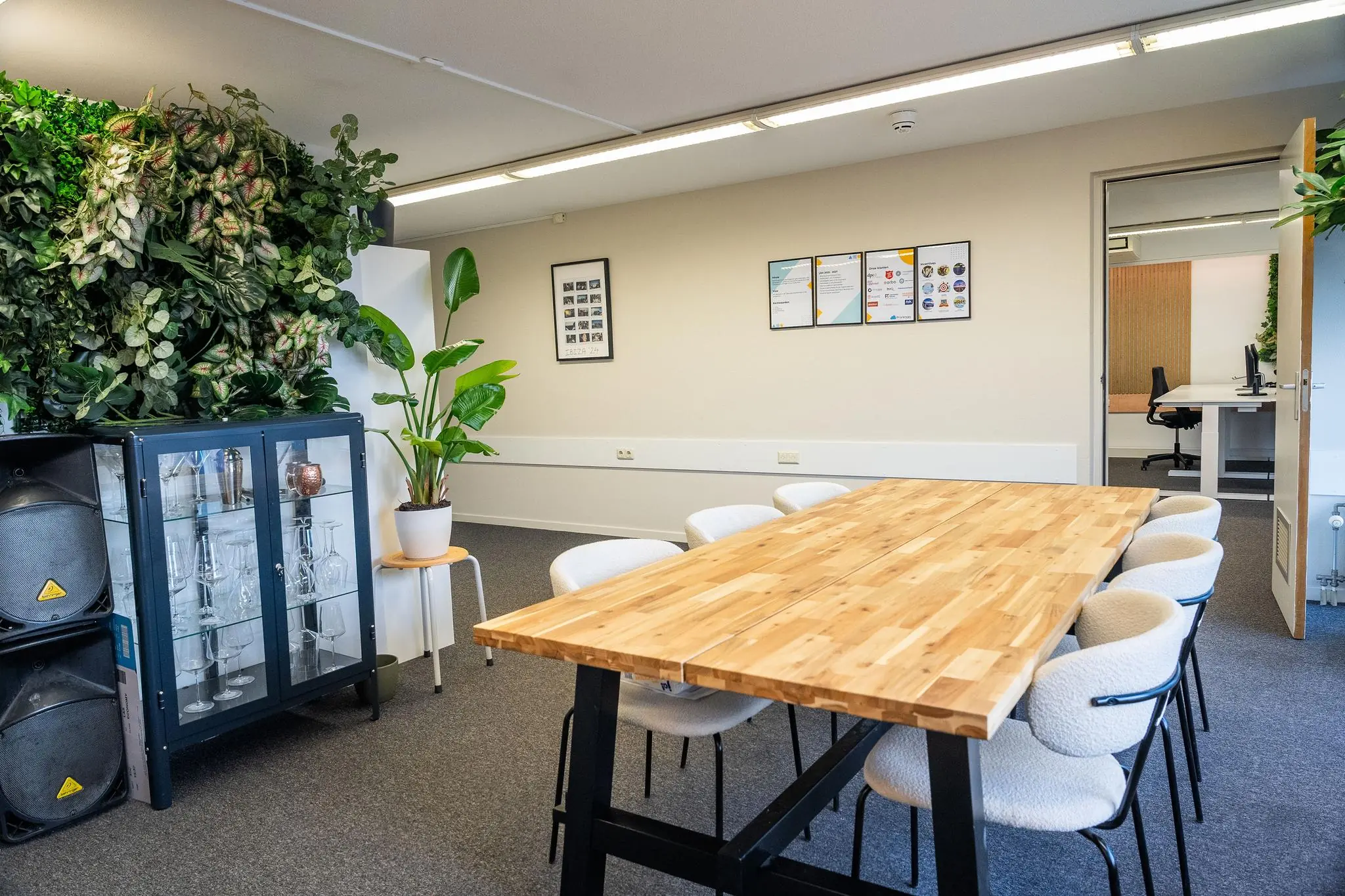 Vergaderruimte aan de Prins Hendrikkade met een houten tafel, moderne stoelen, veel groen en een open doorgang naar een naastgelegen kantoorruimte.