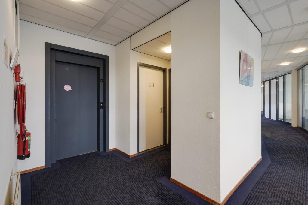 Binnenhal van een kantoorgebouw aan de Laan van S-Gravenmade met een lift, een deur en een gang met glazen kantoorwanden.