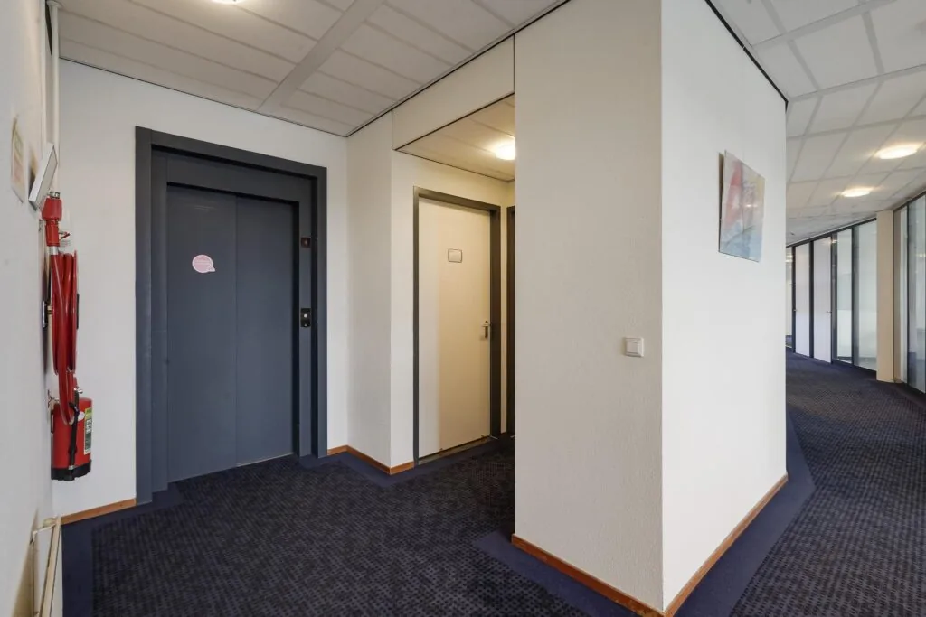 Binnenhal van een kantoorgebouw aan de Laan van S-Gravenmade met een lift, een deur en een gang met glazen kantoorwanden.