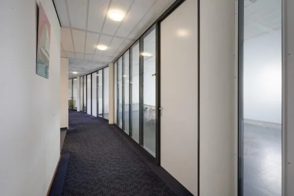 Gang in een modern kantoorpand aan de Laan van ’s-Gravenmade met glazen kantoorwanden en donker tapijt.