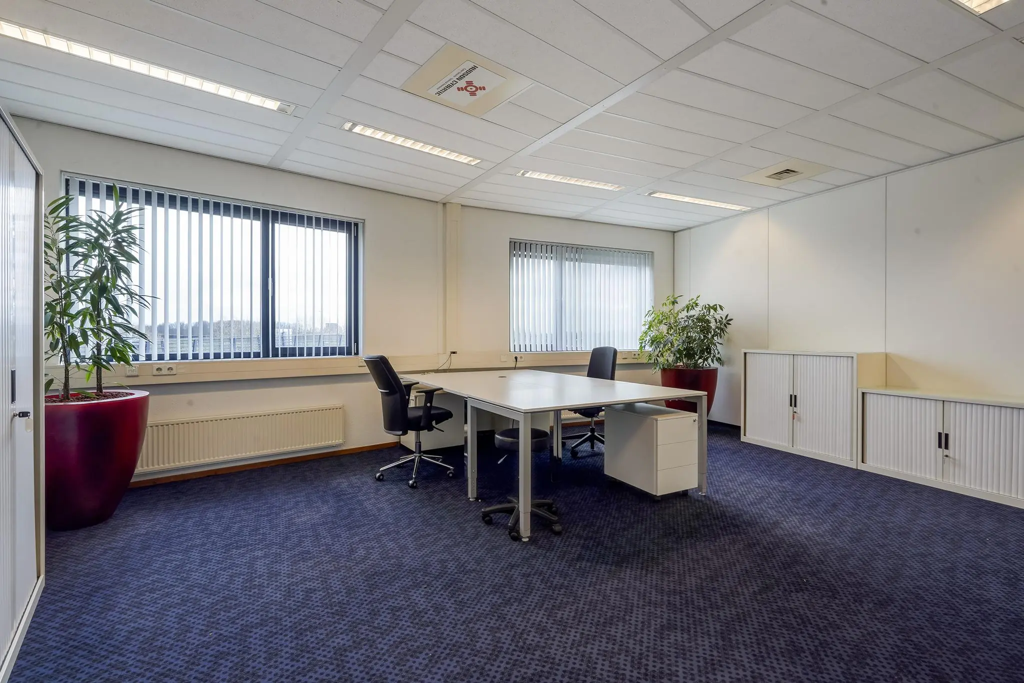 Modern en licht kantoor aan de Laan van 's-Gravenmade met twee bureaus, zwarte bureaustoelen, opbergkasten en grote planten in rode potten.