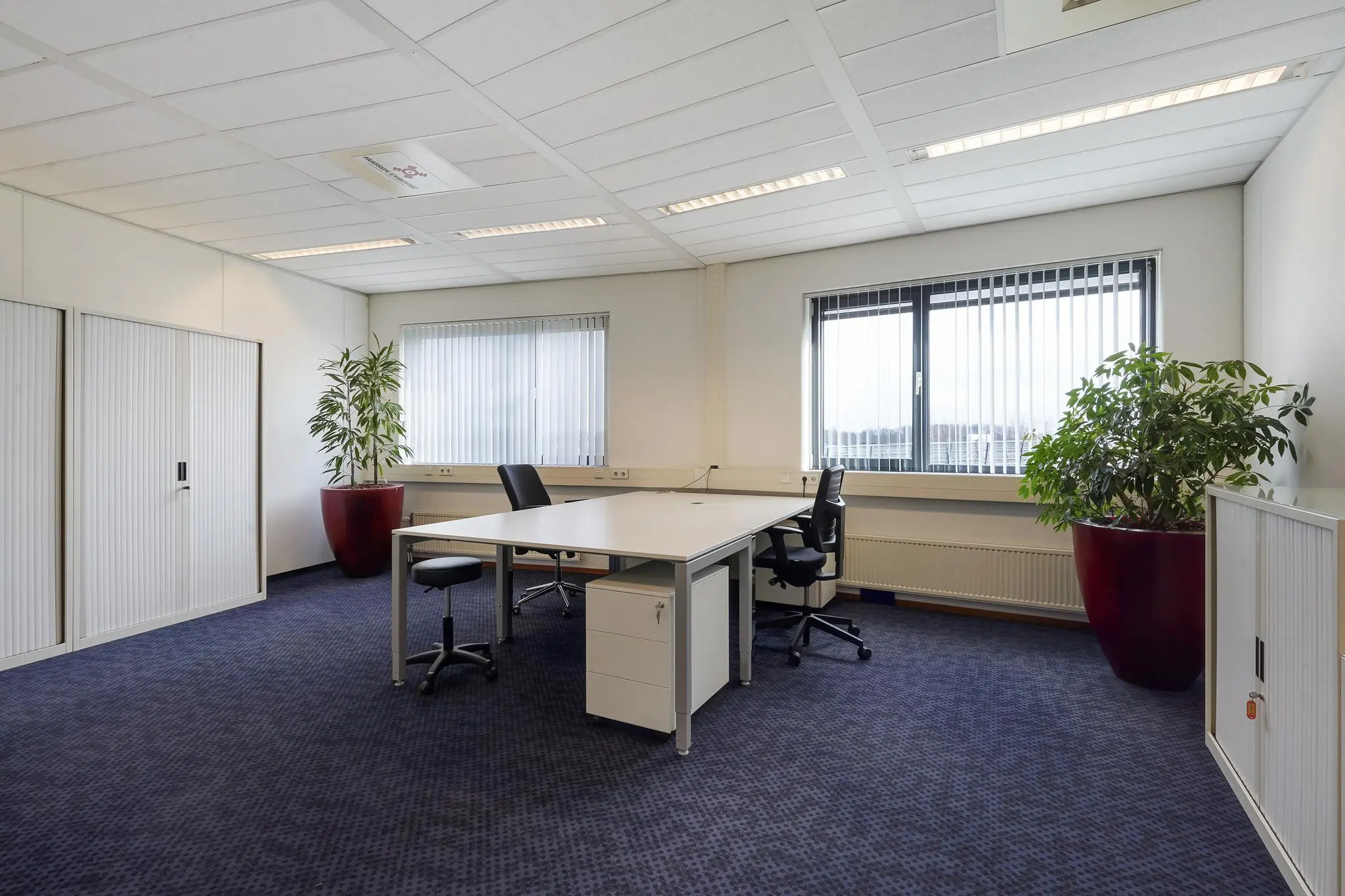 Modern kantoor met twee bureaus, kantoorstoelen, opbergkasten en grote planten, gelegen aan de Laan van S-Gravenmade.