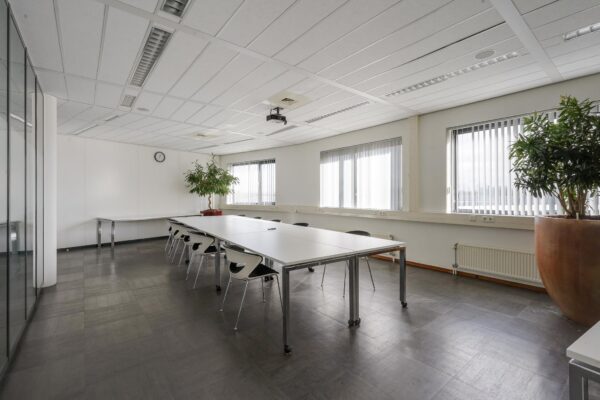 Vergaderruimte met lange tafels, moderne stoelen, grote planten en veel daglicht aan de Laan van ’s-Gravenmade.