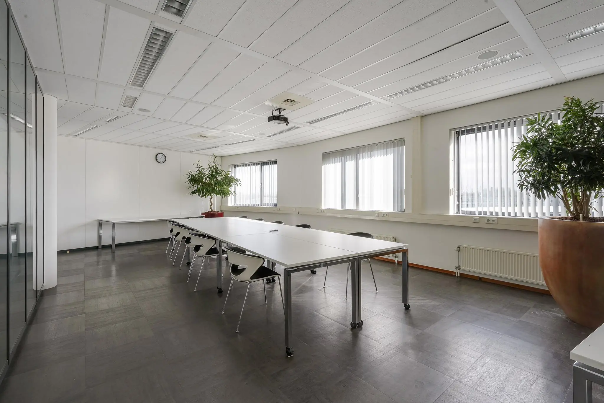 Vergaderruimte met lange tafels, moderne stoelen, grote planten en veel daglicht aan de Laan van ’s-Gravenmade.