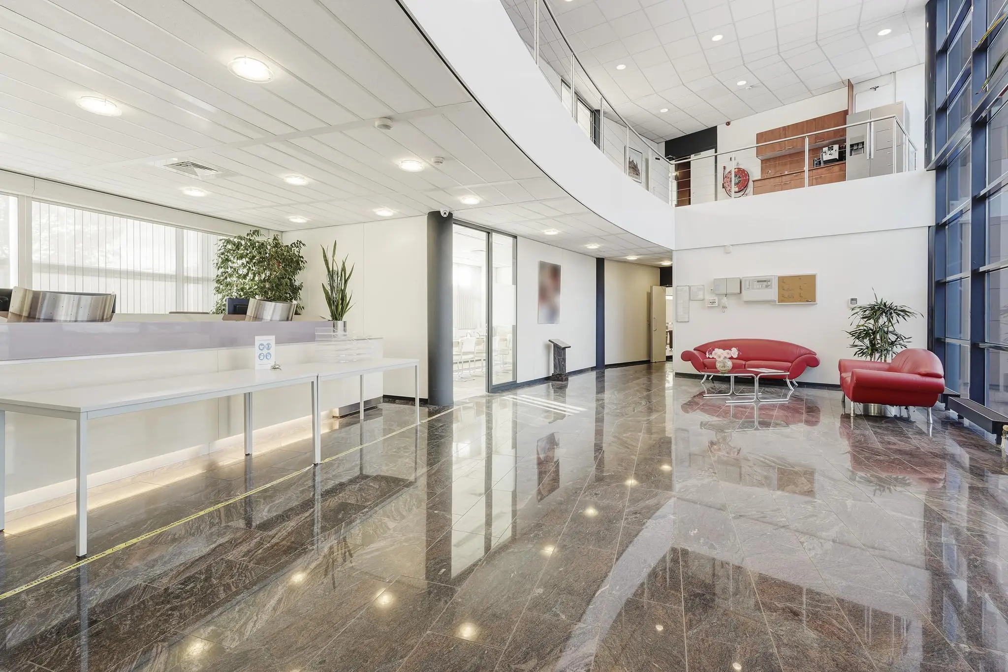 Moderne, lichte ontvangsthal aan de Laan van ’s-Gravenmade met glanzende marmeren vloer, rode zitbanken en een receptiebalie.