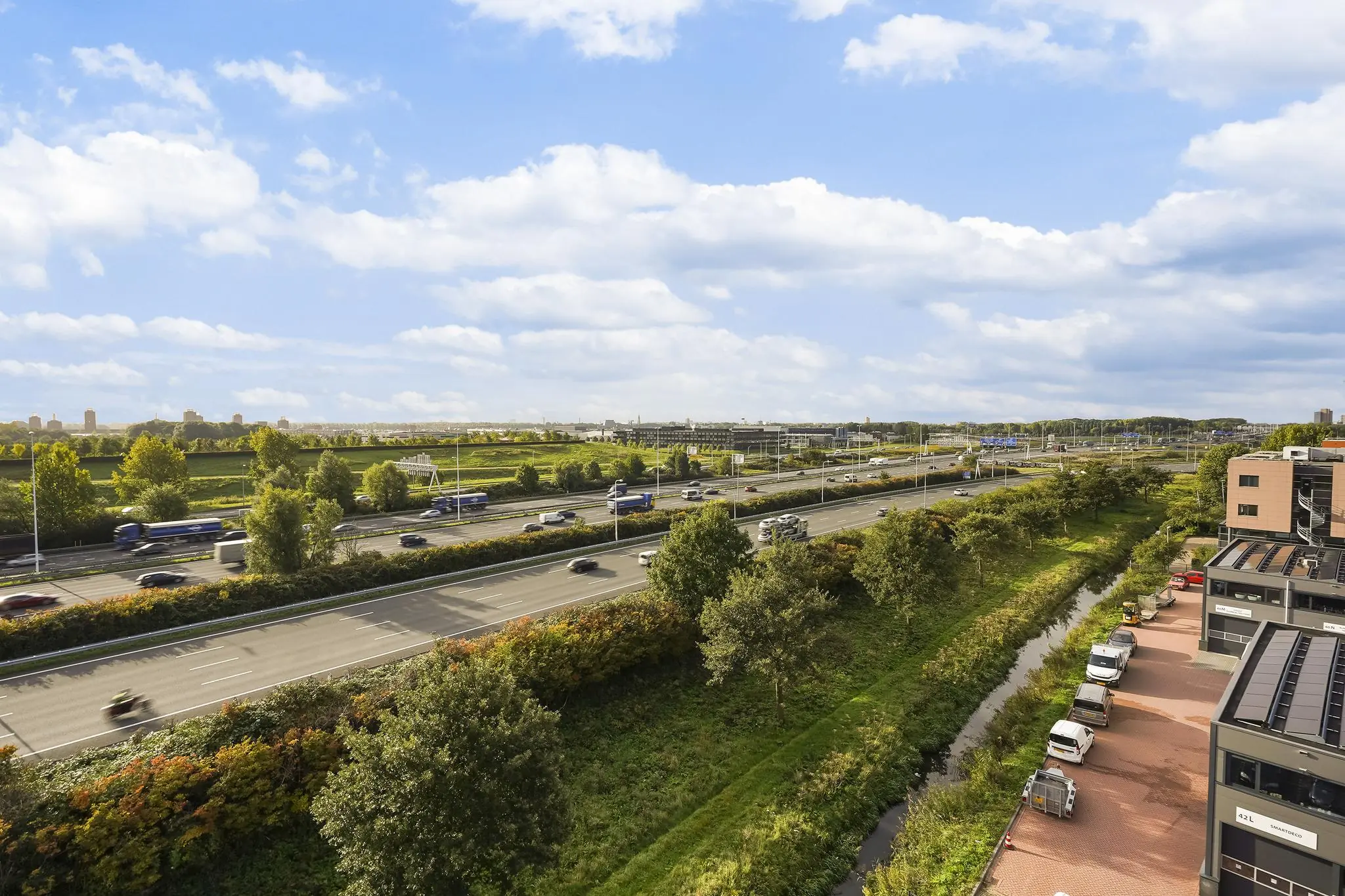 Drukke snelweg langs de Laan van ’s-Gravenmade met omliggend groen en kantoorgebouwen.