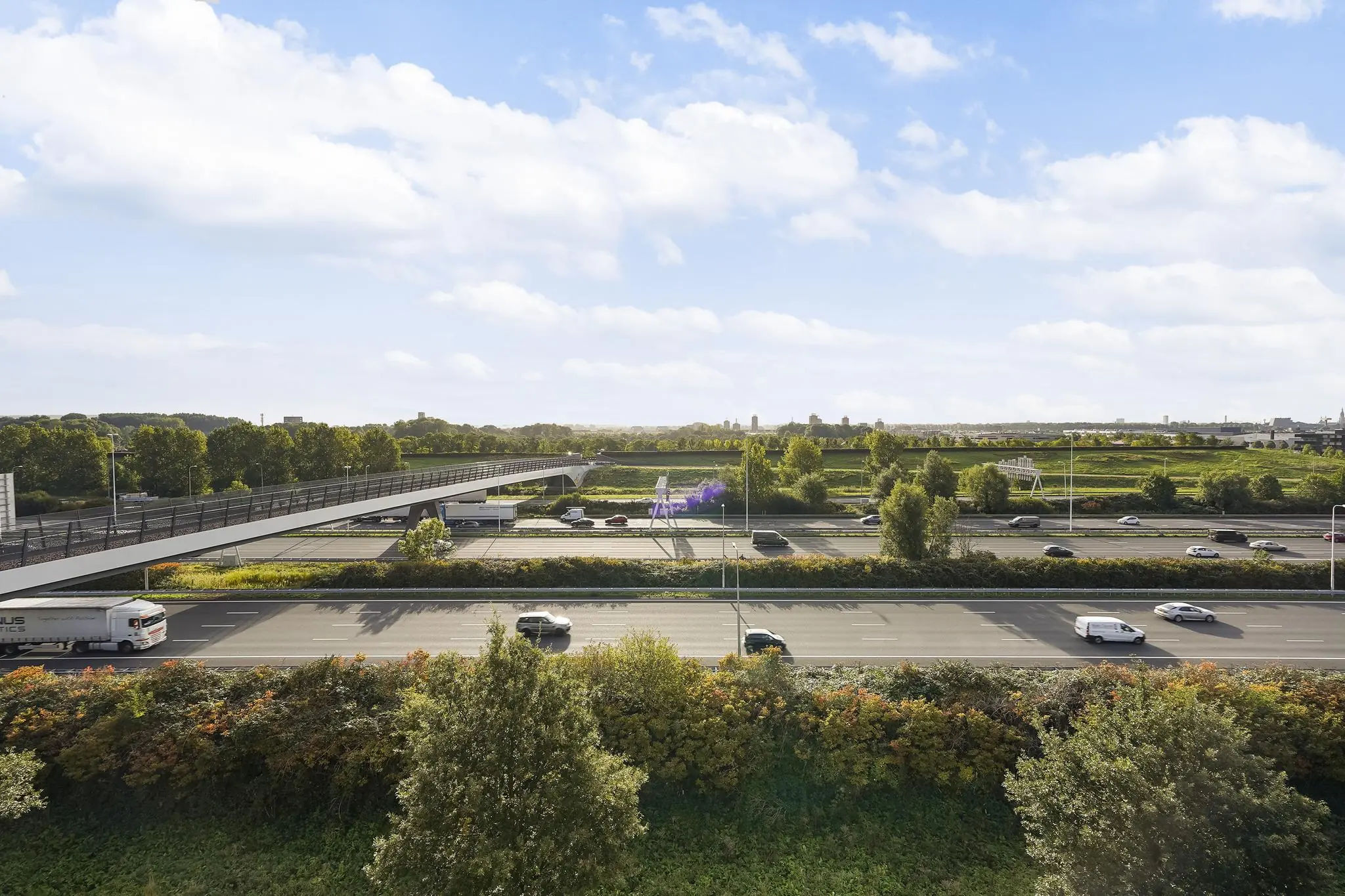 Fietsbrug over de snelweg bij Laan van S-Gravenmade met uitzicht op groen landschap en verkeer.