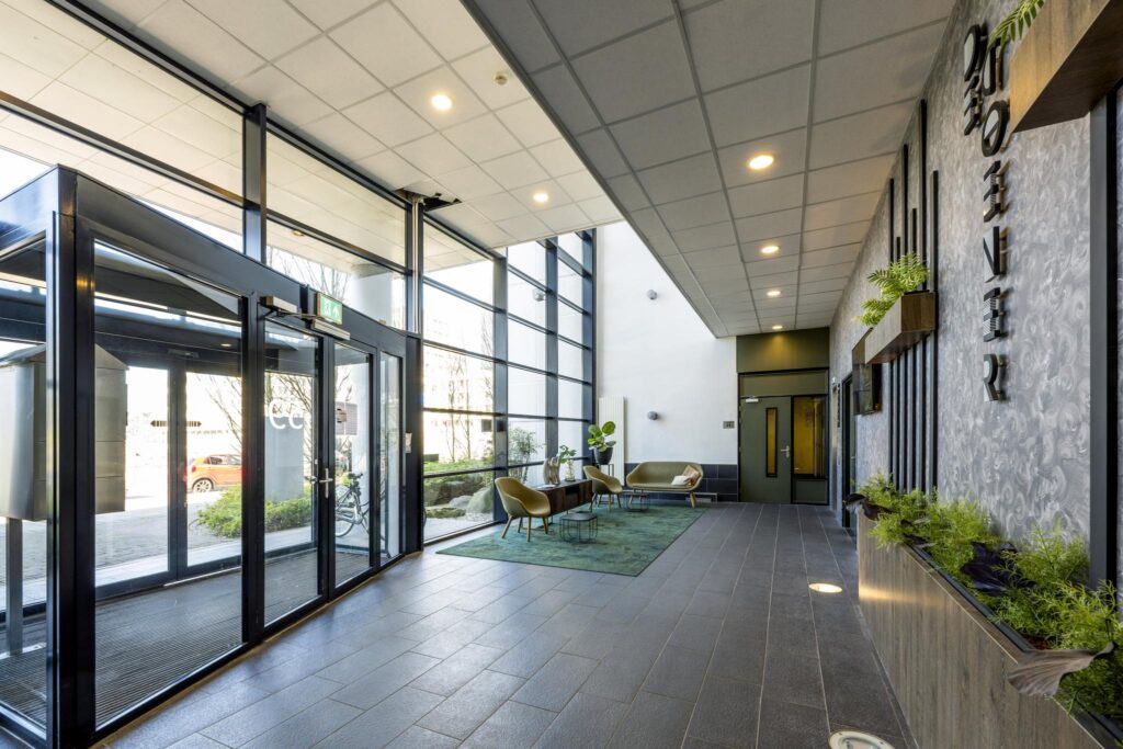 Moderne entreehal van een kantoorpand aan de Overschiestraat met grote glazen pui, zitgedeelte en groene accenten.