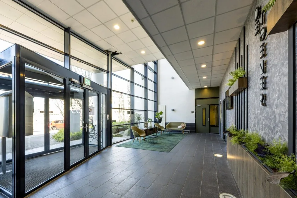 Moderne entreehal van een kantoorpand aan de Overschiestraat met grote glazen pui, zitgedeelte en groene accenten.