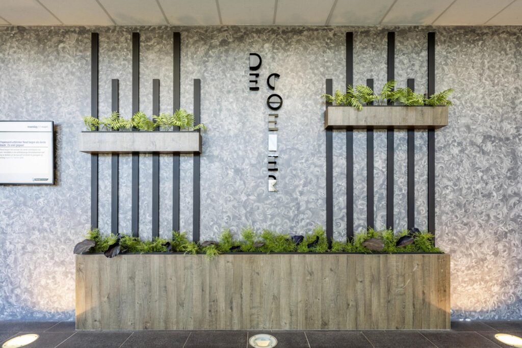 Moderne muurdecoratie met plantenbakken en verticale zwarte lamellen in de entree van het gebouw aan de Overschiestraat.