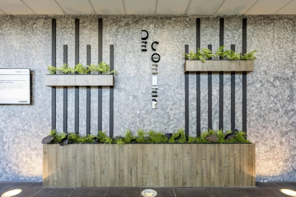 Moderne muurdecoratie met plantenbakken en verticale zwarte lamellen in de entree van het gebouw aan de Overschiestraat.