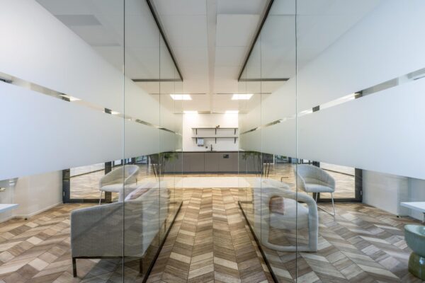 Moderne kantoorpauzeruimte aan de Overschiestraat met glazen wanden, houten visgraatvloer en minimalistisch interieur.