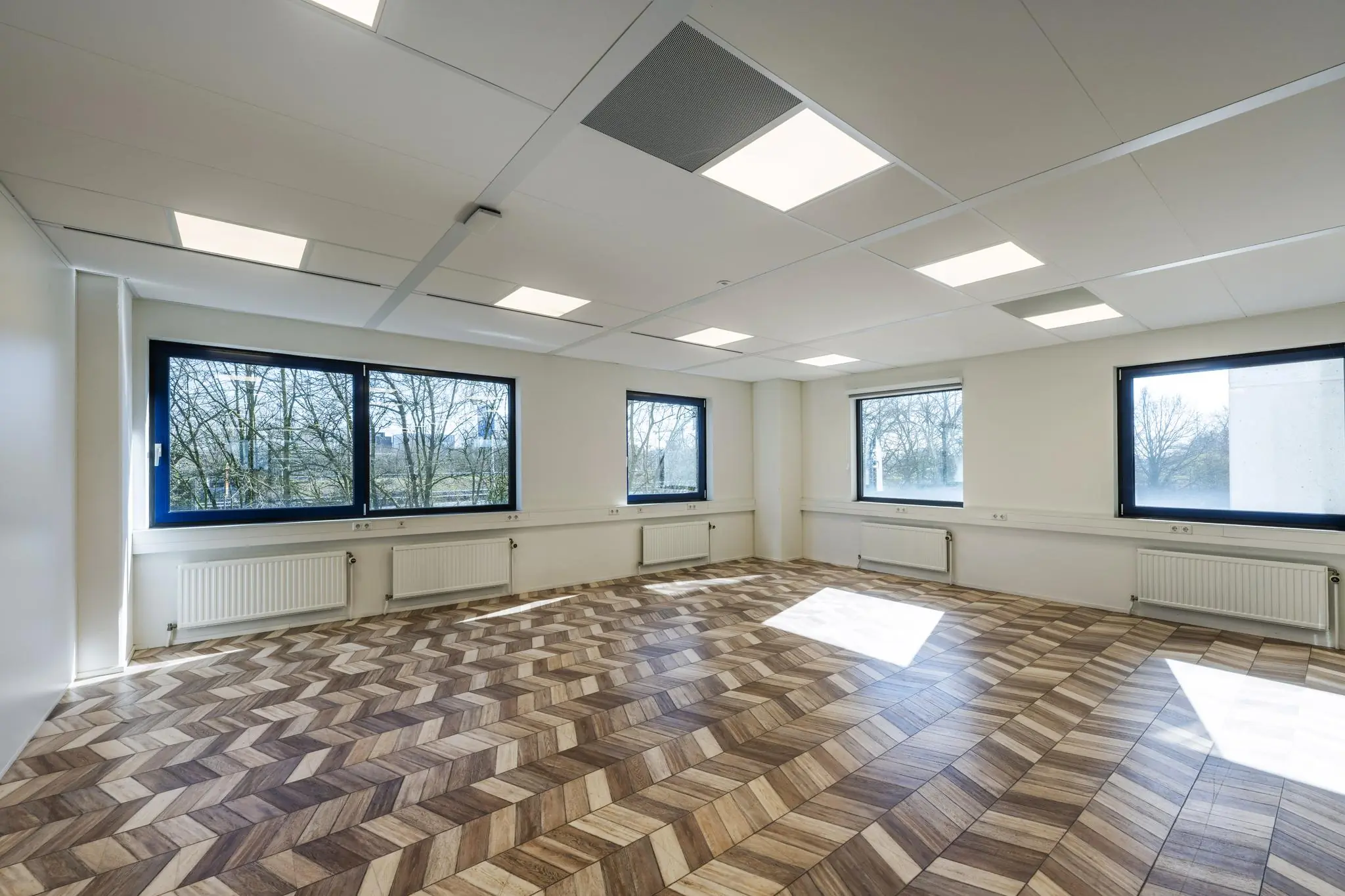 Licht en ruim kantoor aan de Overschiestraat met grote ramen en een opvallende houten visgraatvloer.