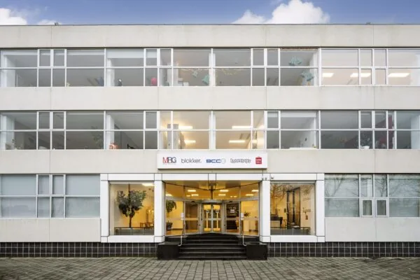 Vooraanzicht van een kantoorpand aan de Van der Madeweg met bedrijfsnamen Blokker, BCC, Intertoys, MRG en Miniso op de gevel.
