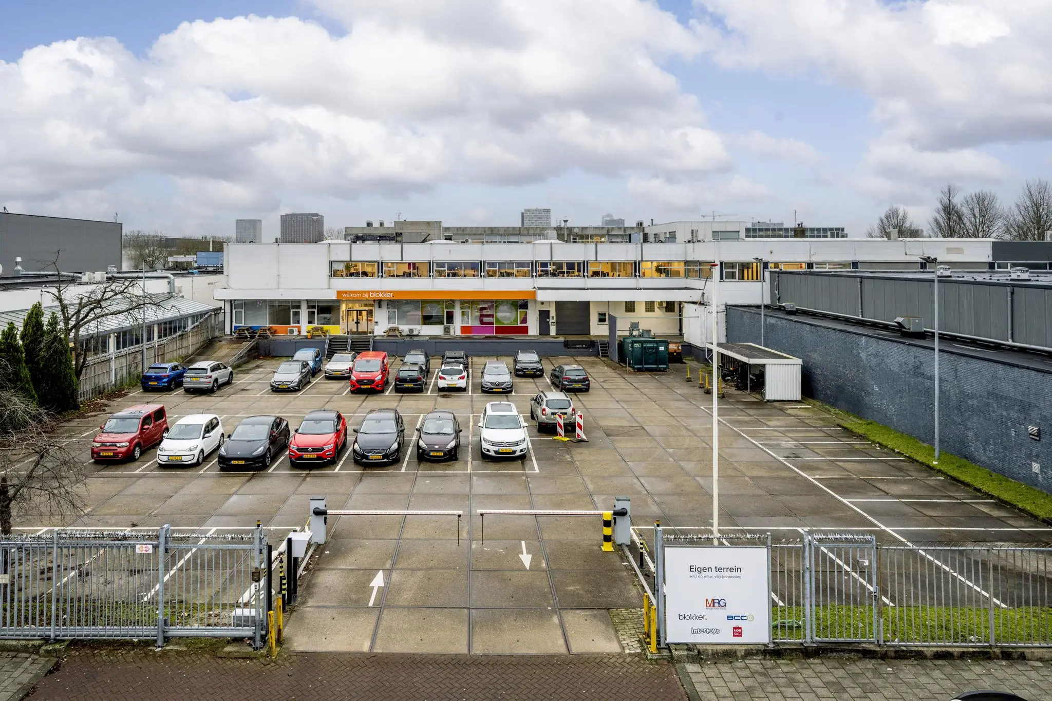 Parkeerterrein met meerdere auto's voor het bedrijventerrein aan de Van der Madeweg, met op de achtergrond een Blokker-pand.