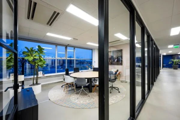 Moderne vergaderruimte aan de Van der Madeweg met grote ramen, ronde tafel en diverse stoelen op een sfeervol vloerkleed.