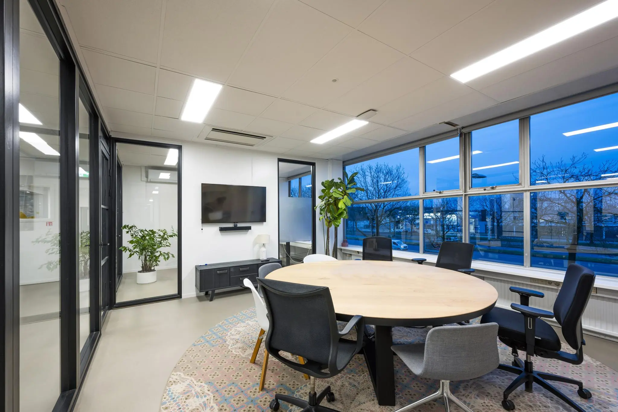 Moderne vergaderruimte aan de Van der Madeweg met ronde tafel, bureaustoelen, grote ramen en een flatscreen aan de muur.