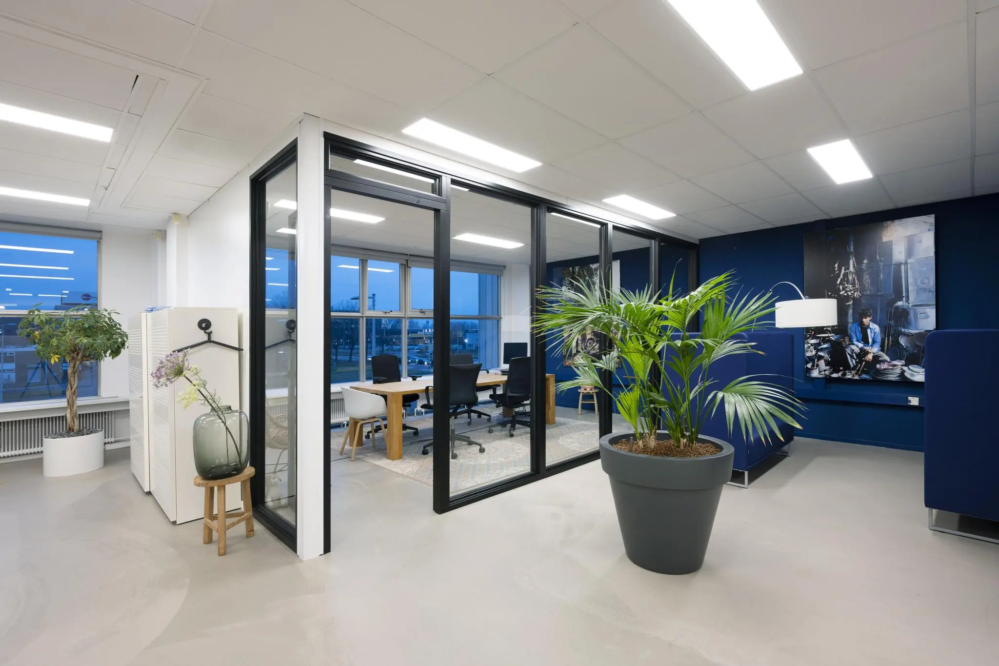 Modern kantoorinterieur aan de Van der Madeweg met glazen vergaderruimte, grote planten en kunst aan de muur.