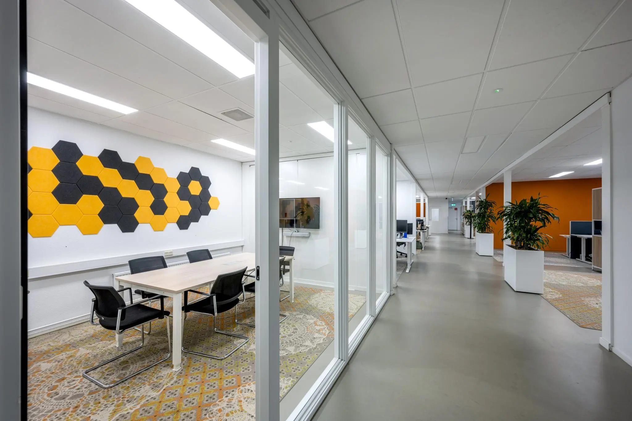Moderne kantoorruimte aan de Van der Madeweg met glazen vergaderruimtes, kleurrijke akoestische wandpanelen en open werkplekken.