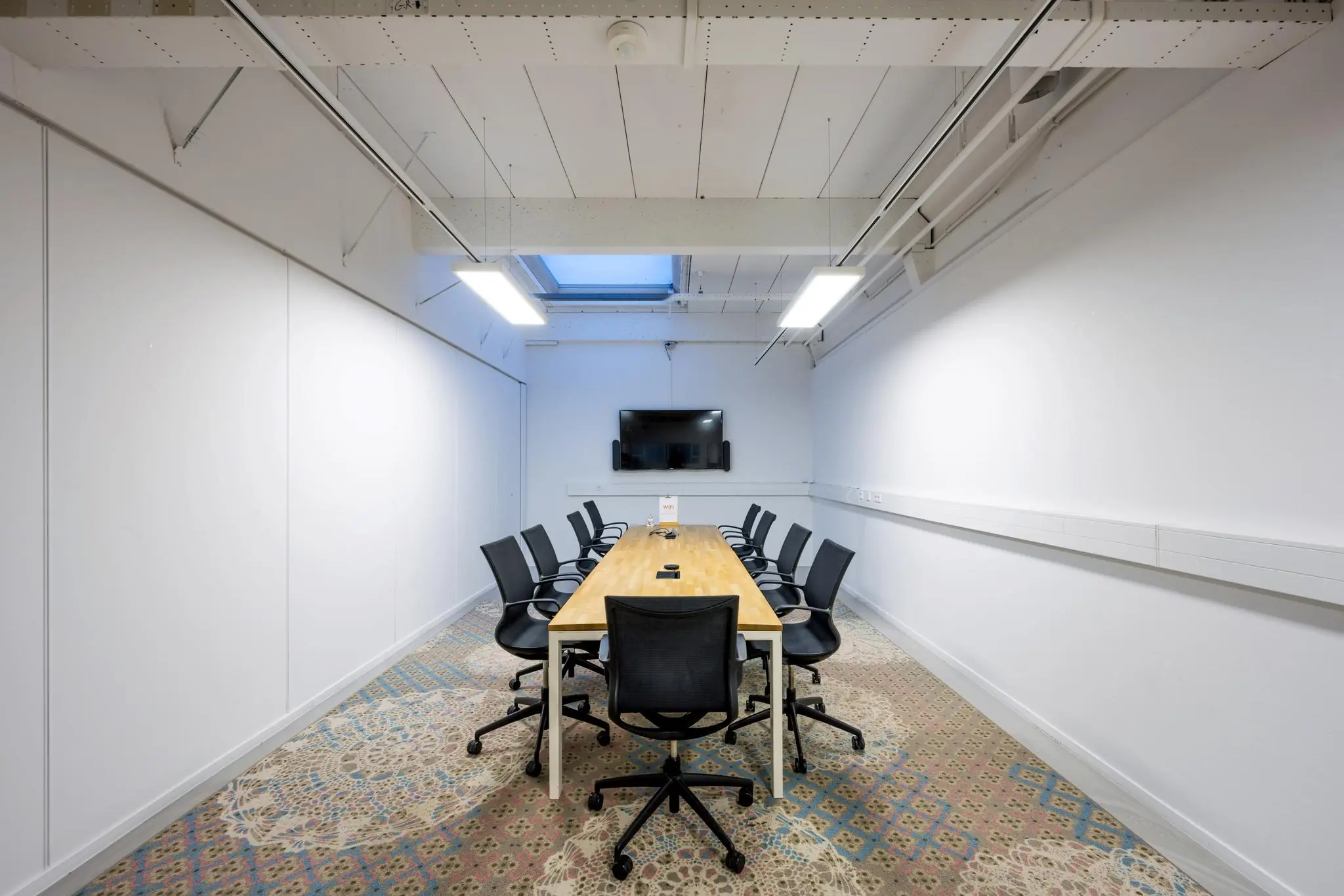 Vergaderruimte aan de Van der Madeweg met een lange houten tafel, twaalf bureaustoelen, tv-scherm en kleurrijk patroon op het tapijt.
