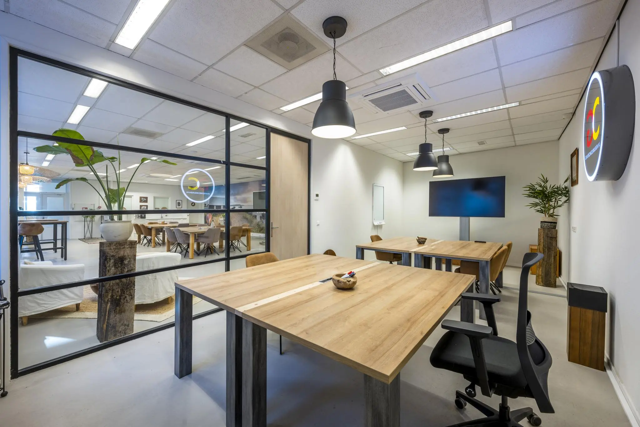 Moderne vergaderruimte aan de Helicopterstraat met houten tafels, designstoelen en glazen wand naar een gemeenschappelijke ruimte.
