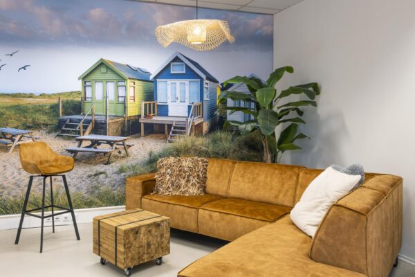 Gezellige zithoek met bruine bank en strandfoto van kleurrijke strandhuisjes op de muur.
