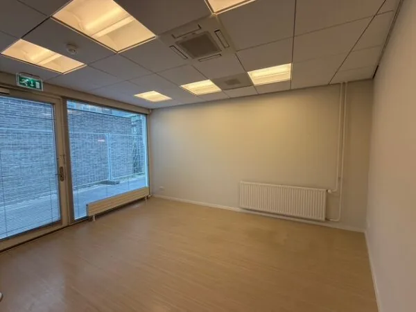 Lege kantoorruimte aan de Fonteynenburghlaan met houten vloer, systeemplafond en groot raam met deur naar buiten.