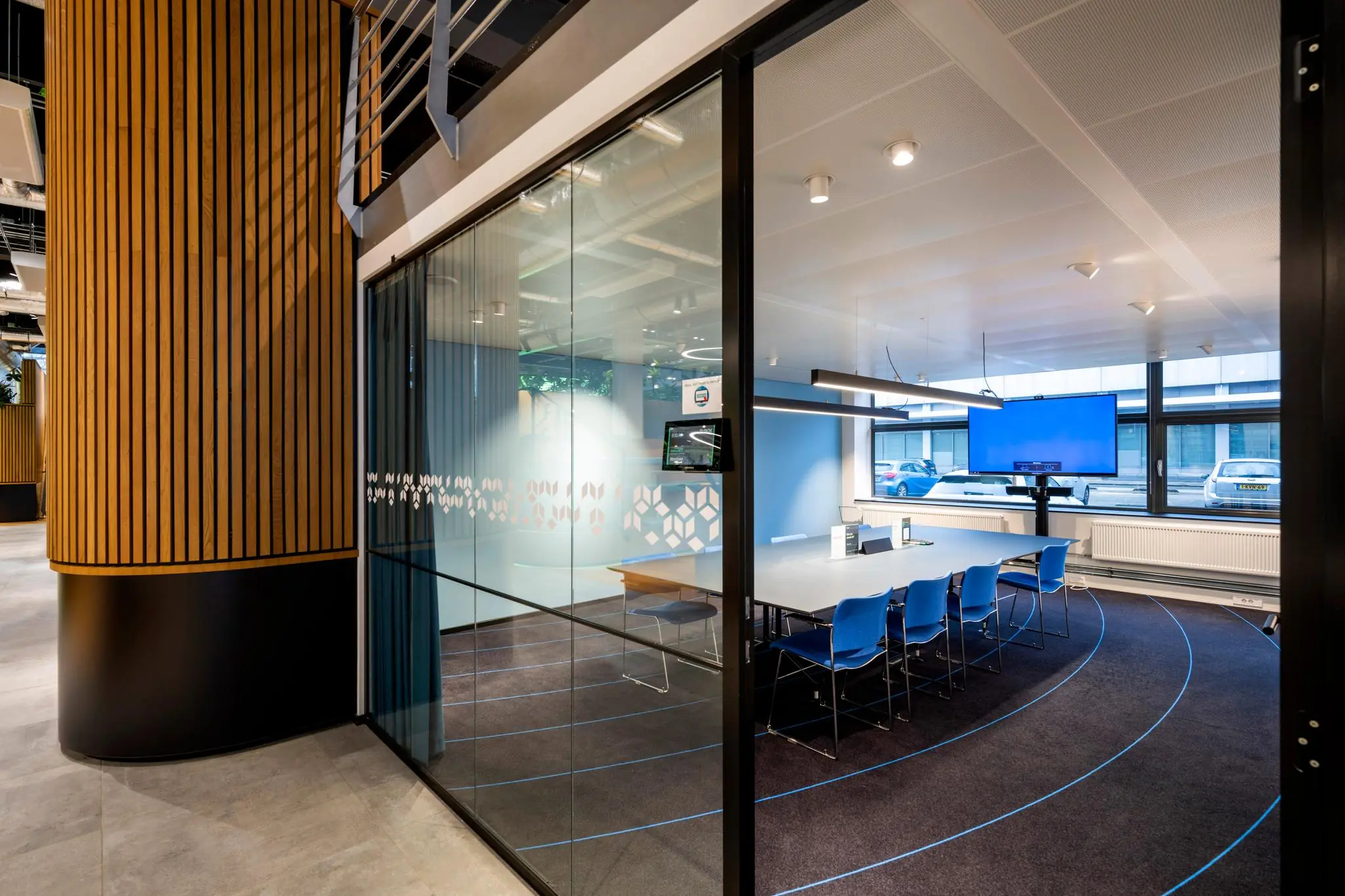 Glazen vergaderruimte aan de Kabelweg met een moderne inrichting, blauwe stoelen en een groot presentatiescherm.